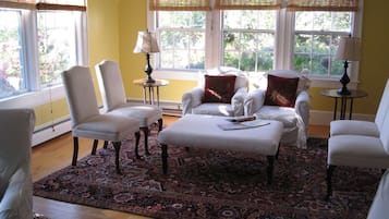 Una habitación con un ventanal grande, un tapete estampado y un sofá blanco con un cojín rojo.
