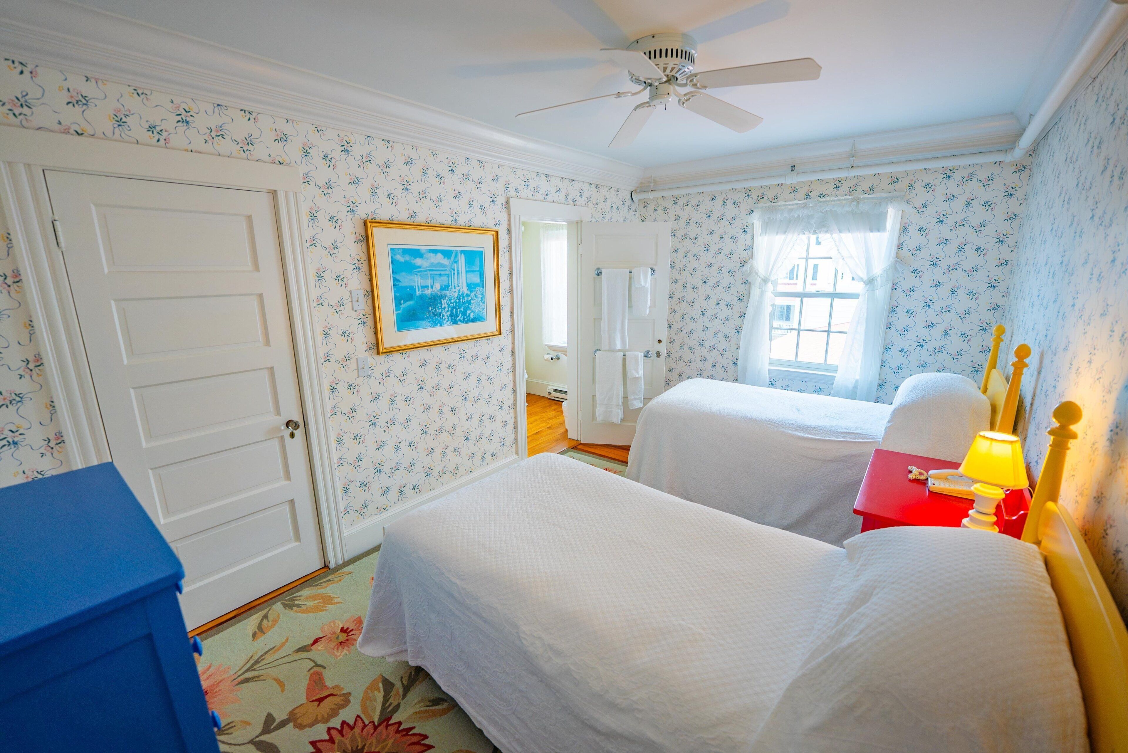 A bedroom with two beds, a ceiling fan, a window with curtains, and a door.