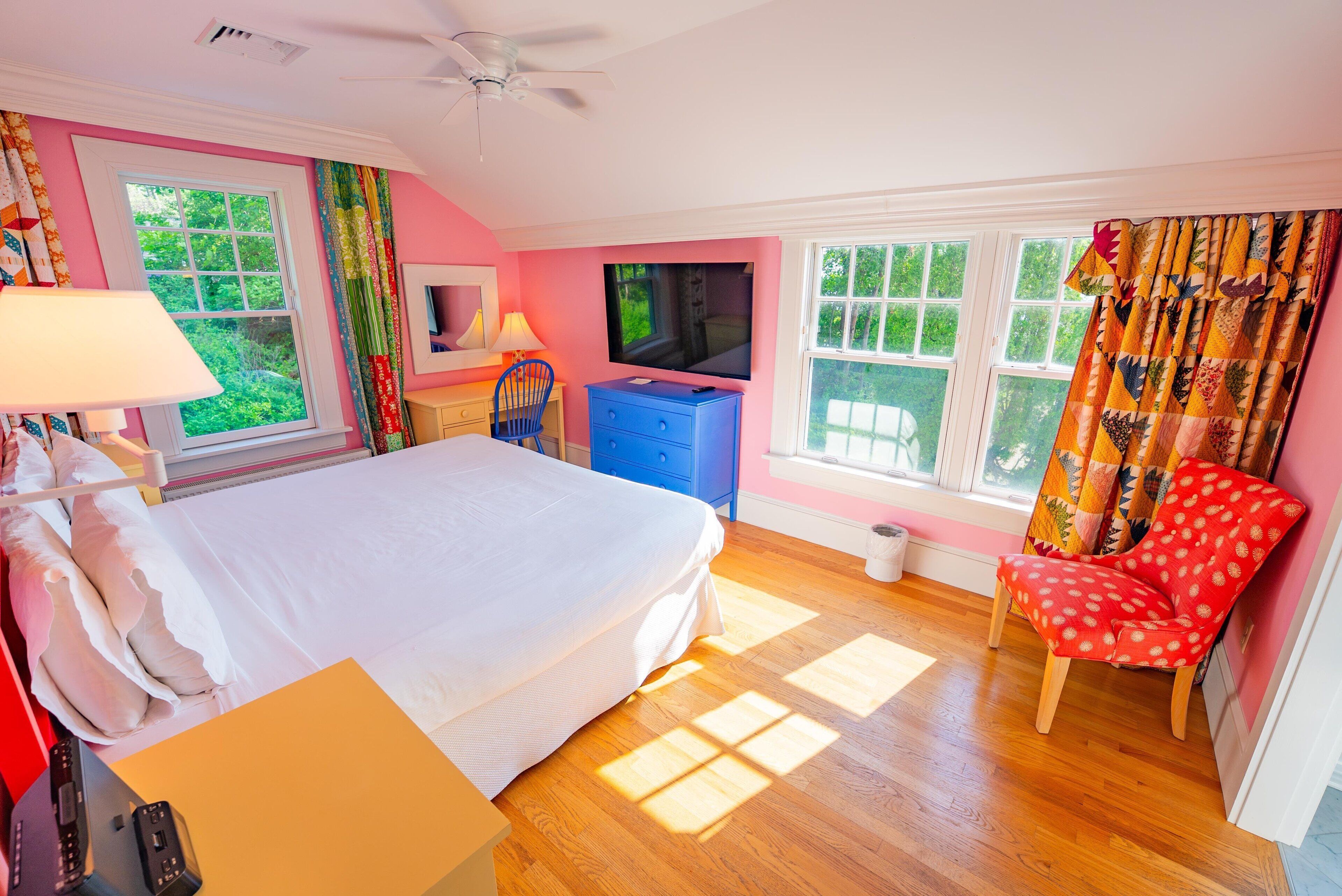 A bedroom with a bed, a TV, a desk, a chair, and a window with curtains.