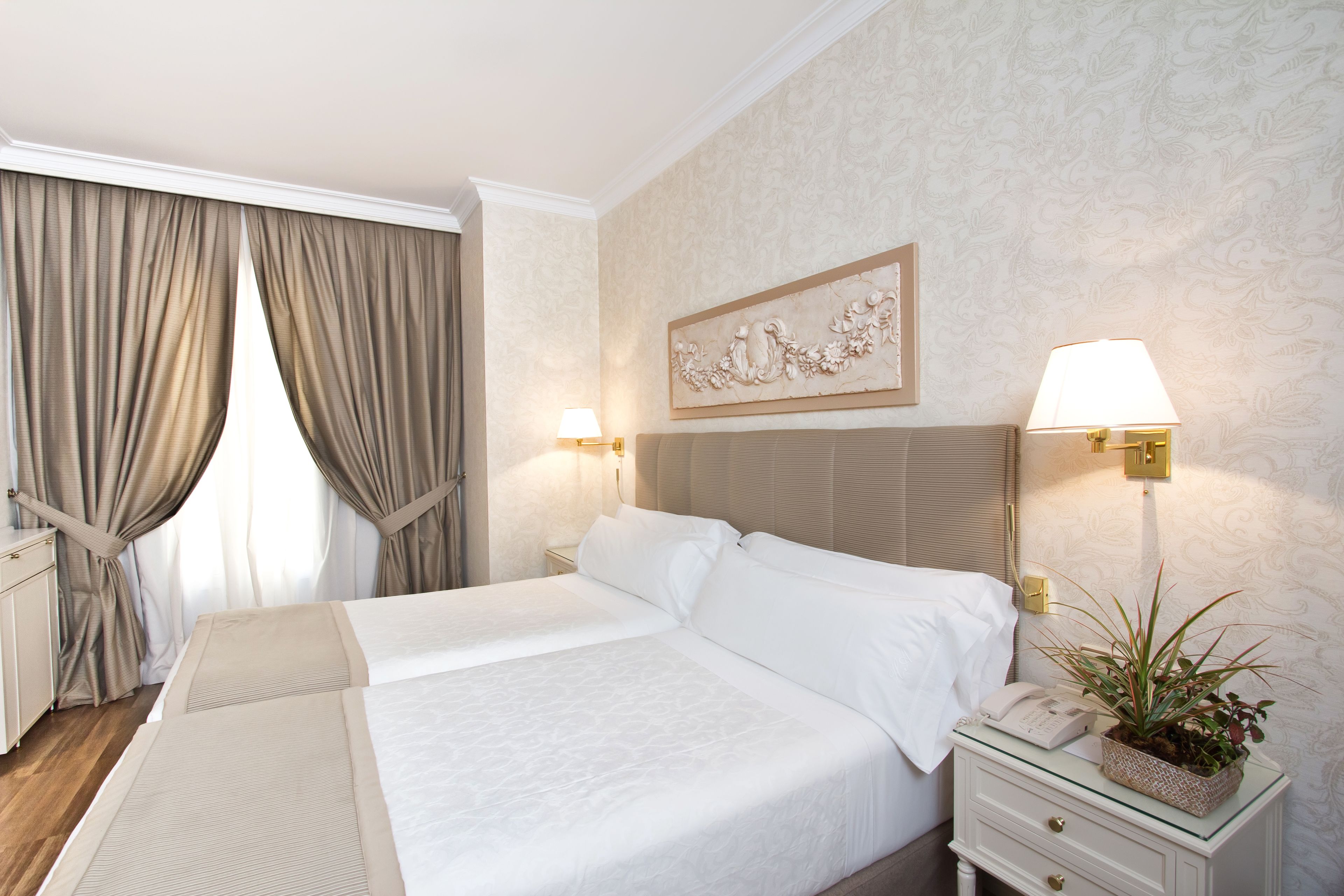 A hotel room with a large bed, a bedside table with a lamp, a phone, and a decorative plant.