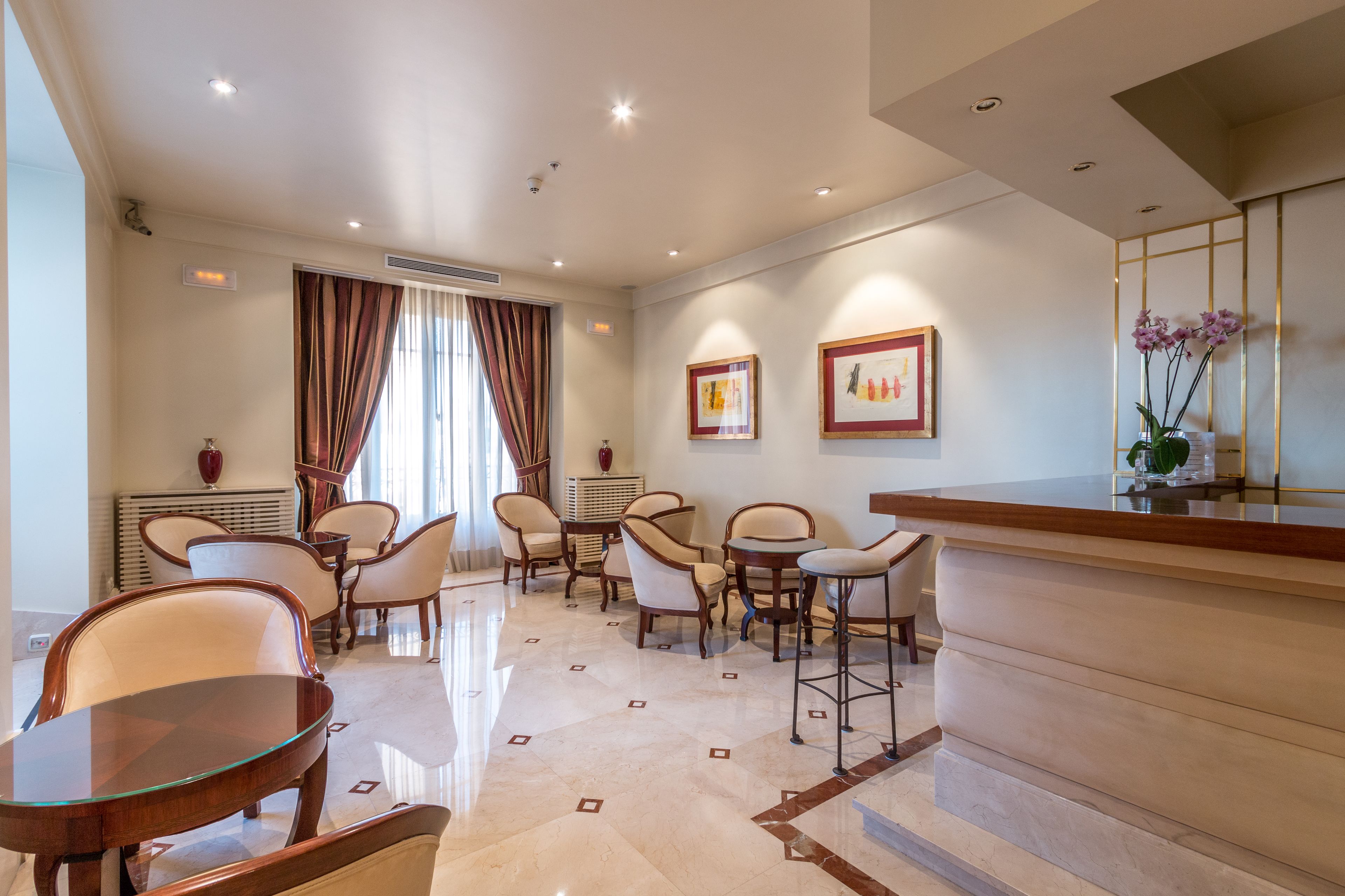Vestíbulo de hotel con mostrador de recepción, área de descanso con sillas y mesas, y obras de arte en las paredes.