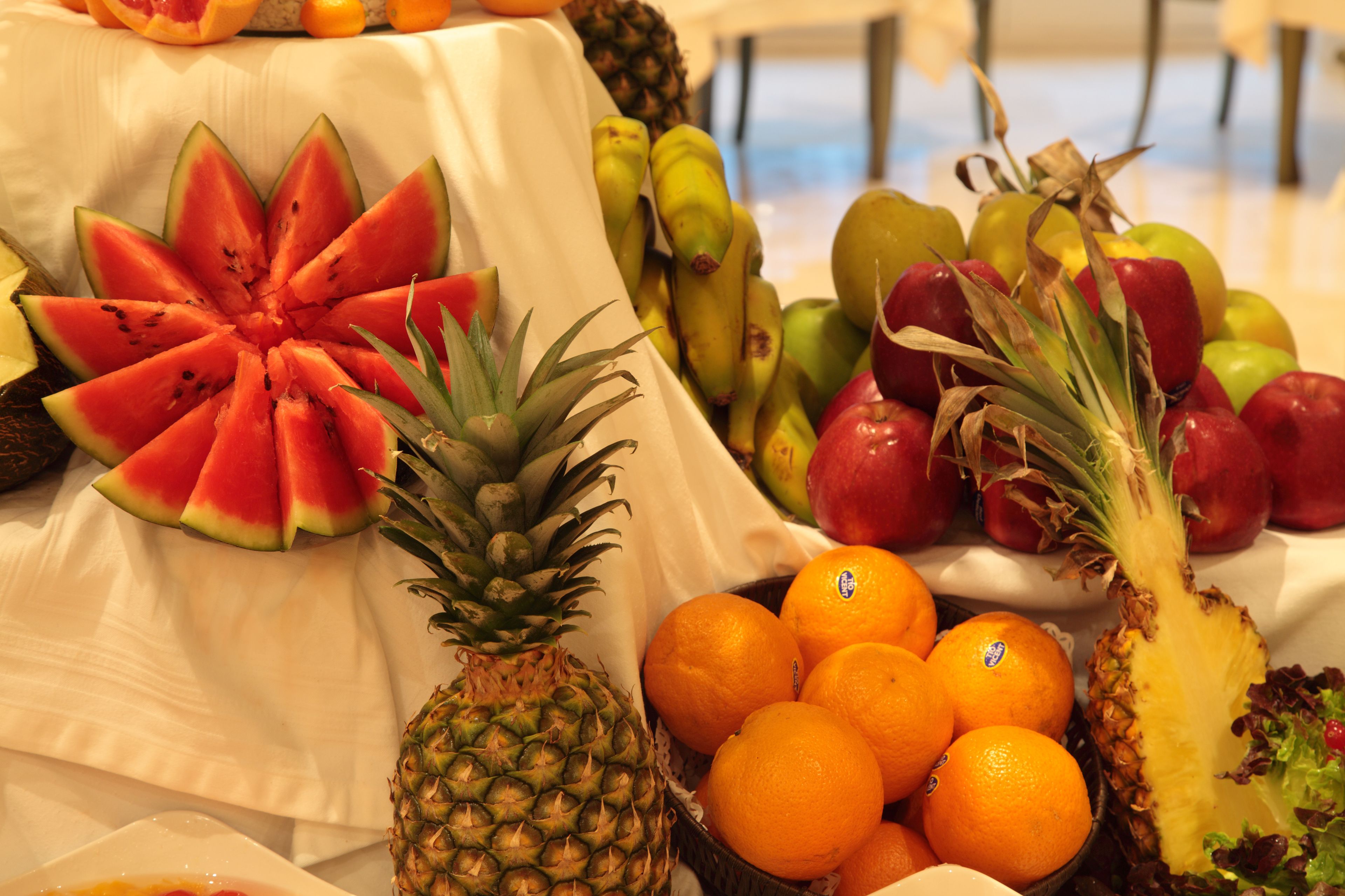 Ein Tisch mit einer Auswahl an Früchten, darunter Wassermelone, Ananas, Orangen und Äpfel.