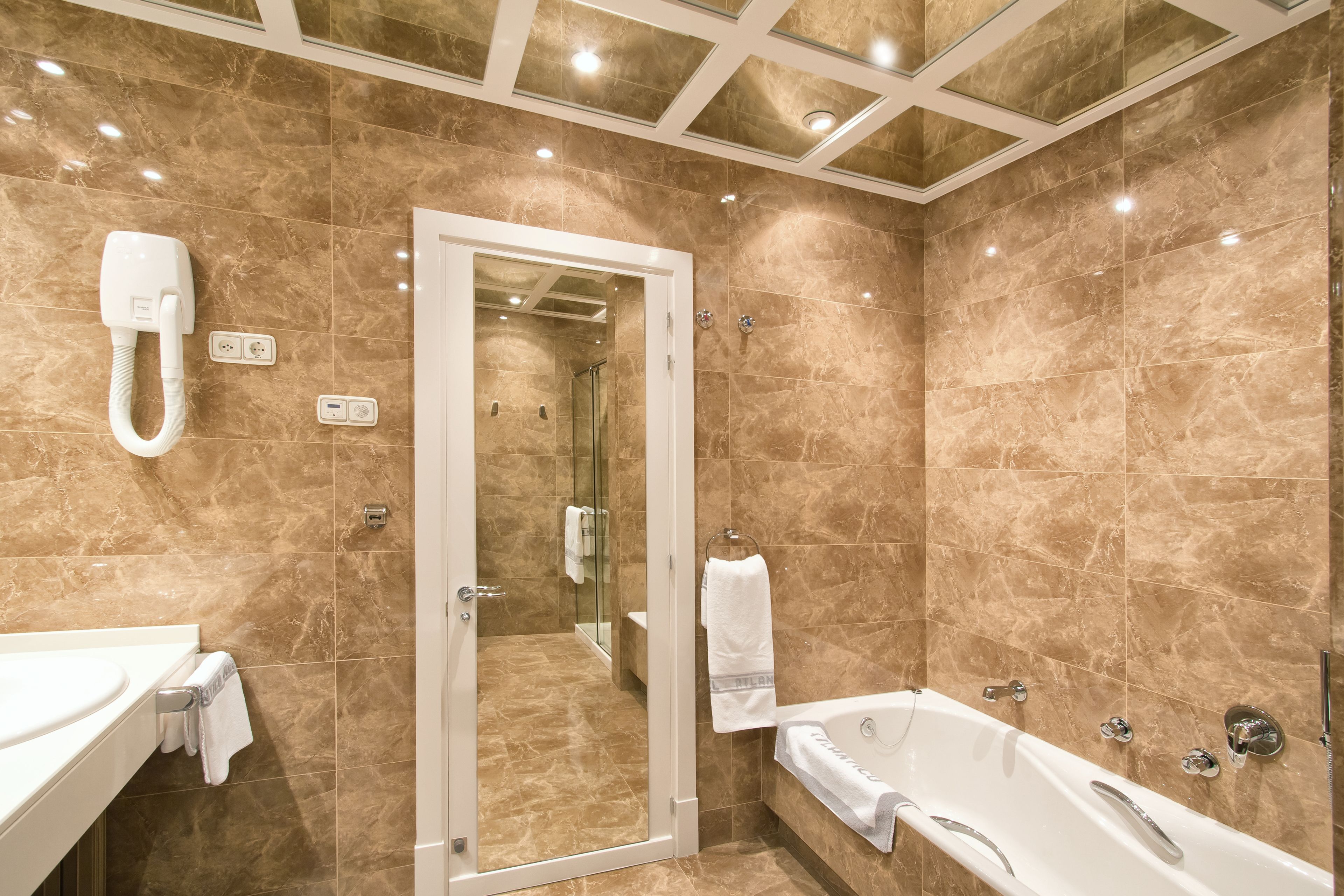 Une salle de bain moderne avec une douche à parois de verre, une baignoire blanche et un meuble-lavabo équipé d’un téléphone.