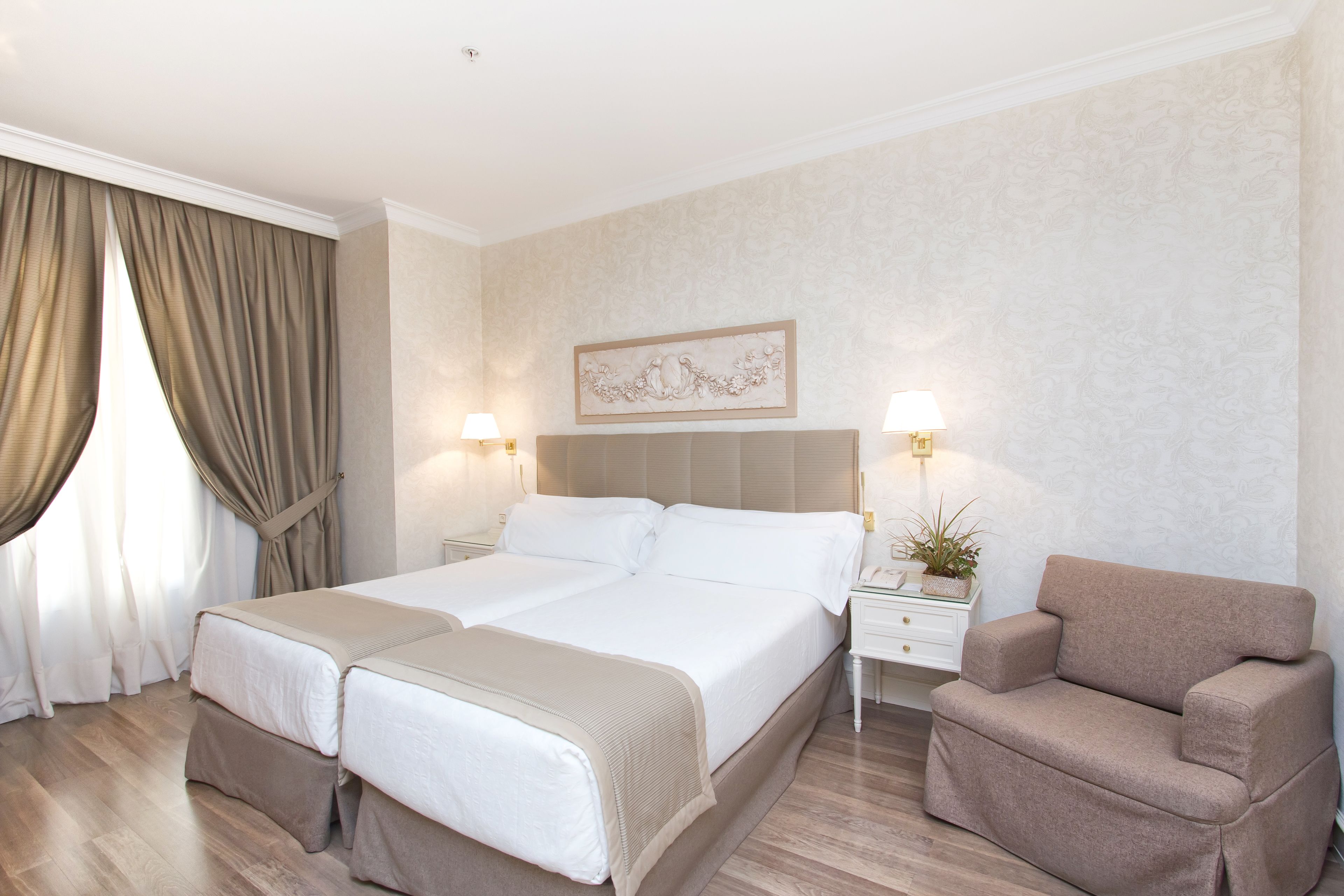 Una habitación de hotel con una cama doble, un sofá, una mesita de noche con lámpara y un elemento decorativo en la pared.
