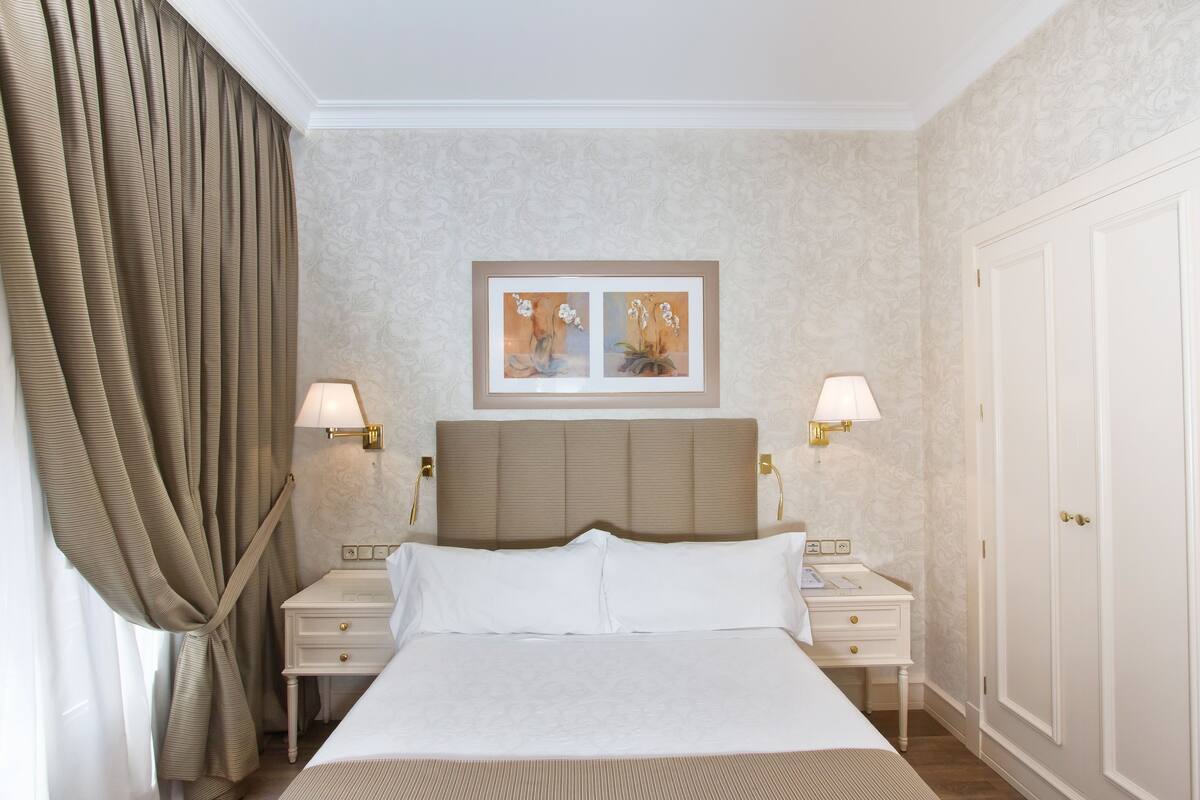 A neatly made bed with white linens, two bedside tables with lamps, a headboard, and a door to the right.
