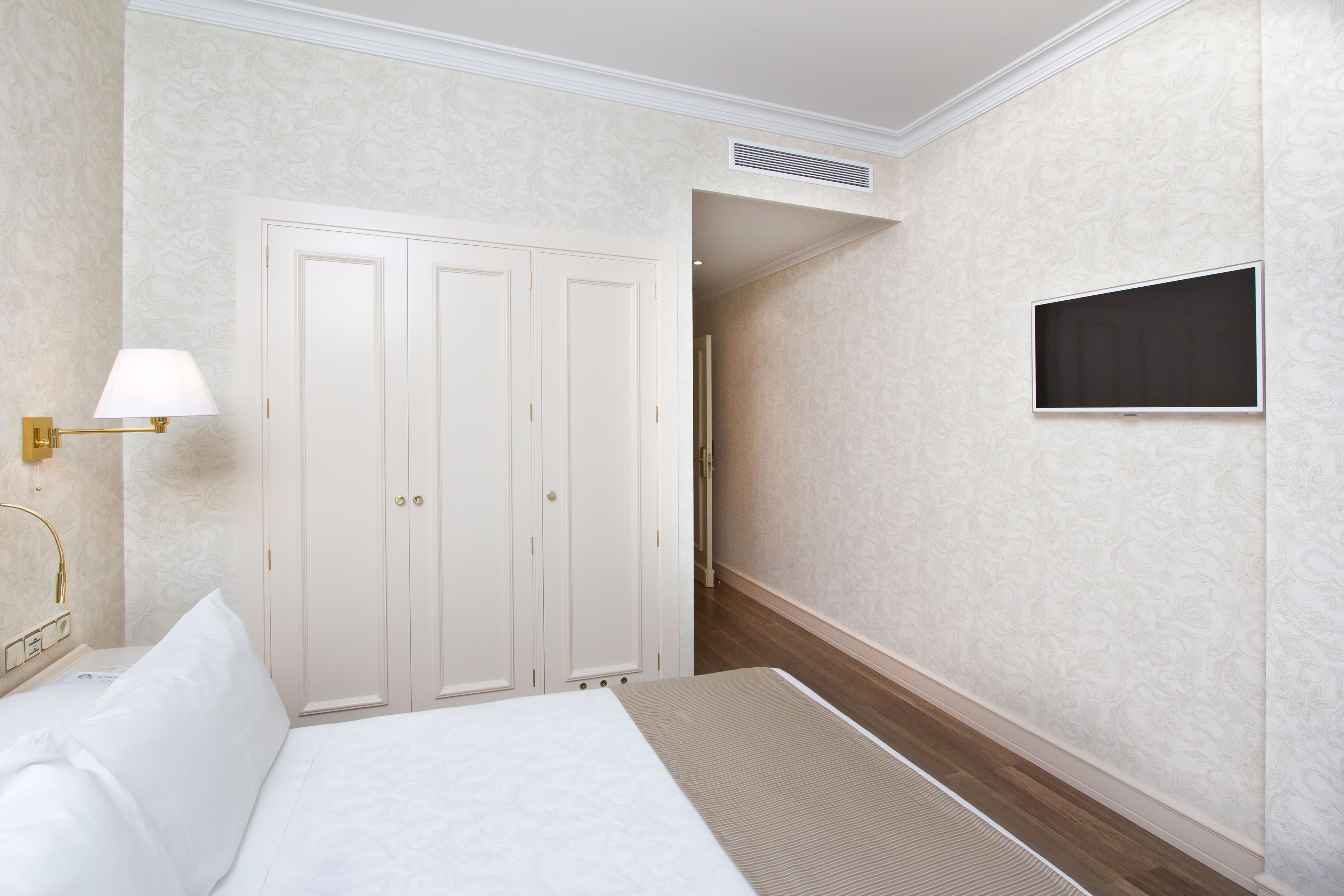 A hotel room with a bed, a wardrobe, a television, and a lamp.