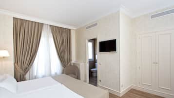 A hotel room with a bed, a TV mounted on the wall, a wardrobe, and a bathroom visible through an open door.