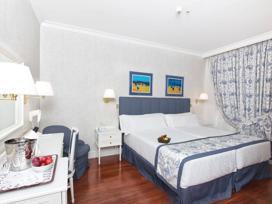 Ein Hotelzimmer mit einem Bett, einem Schreibtisch mit Lampe, einem Sessel, einem Nachttisch und einer Wand mit zwei Bildern in Rahmen.