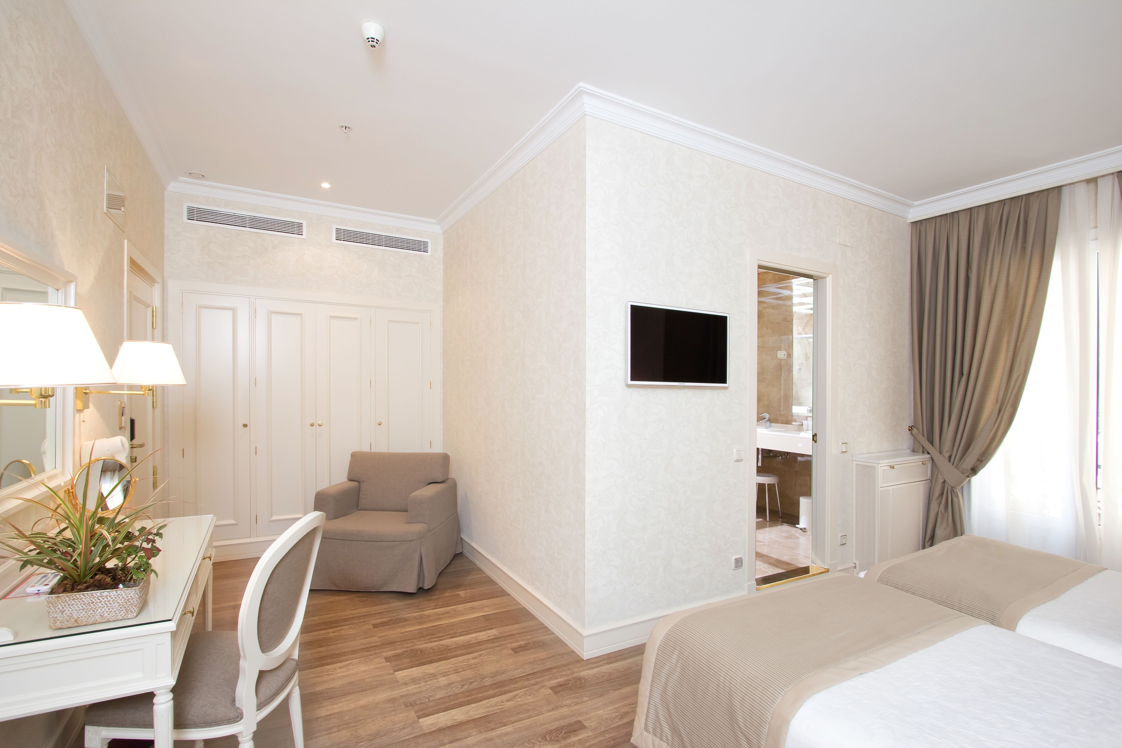 Habitación de hotel con cama, escritorio con silla, televisor montado en la pared y baño visible a través de una puerta abierta.