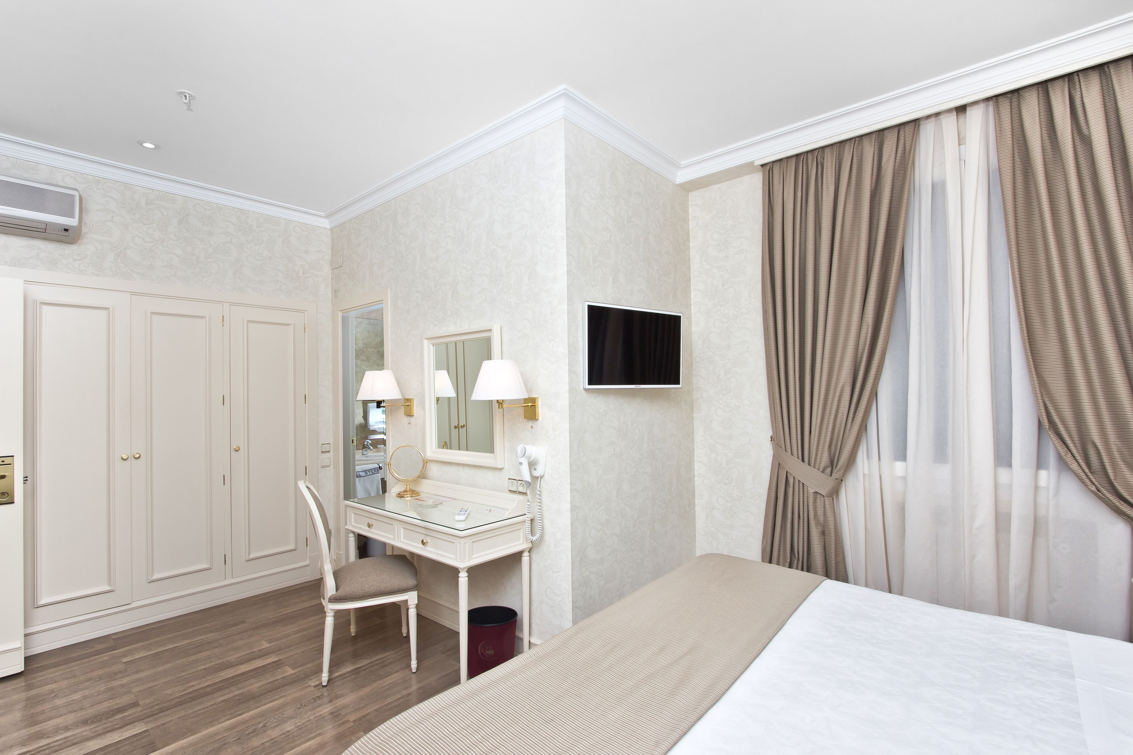 Una camera d'albergo con un letto, una toeletta con specchio, una scrivania e una televisione.