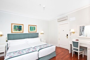 Ein Hotelzimmer mit einem großen Bett, zwei gerahmten Bildern, einem Schreibtisch mit Stuhl und einer Tür.