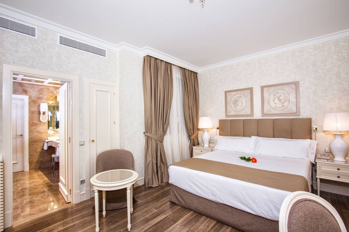 A hotel room with a bed, a chair, a small table, and a bathroom visible through an open door.