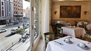 A restaurant with tables set for dining, a large window overlooking a busy street, and a painting on the wall.