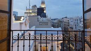 A view through a window with a wrought iron railing, overlooking a cityscape with historic buildings and a clock tower.