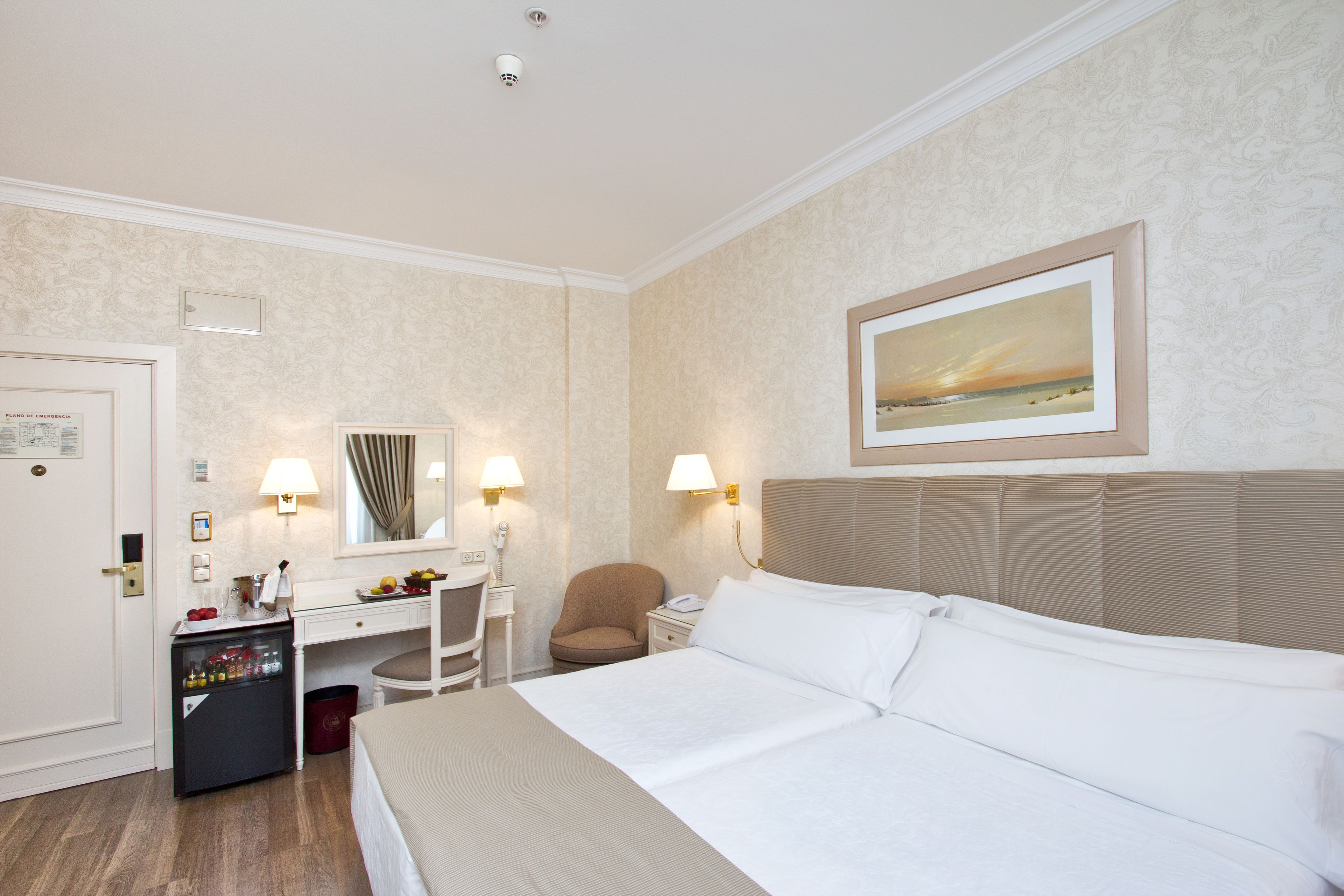 Ein Hotelzimmer mit Bett, Schreibtisch, Stuhl, Minibar und einem Bild an der Wand.