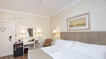 Ein Hotelzimmer mit Bett, Schreibtisch, Stuhl, Minibar und einem Bild an der Wand.