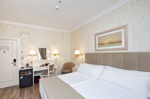 Ein Hotelzimmer mit Bett, Schreibtisch, Stuhl, Minibar und einem Bild an der Wand.