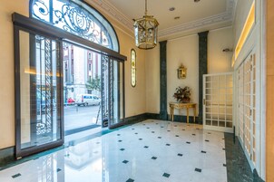 A lobby with a tiled floor, a large glass door with metal framing, a hanging lantern, and a small table with a plant.