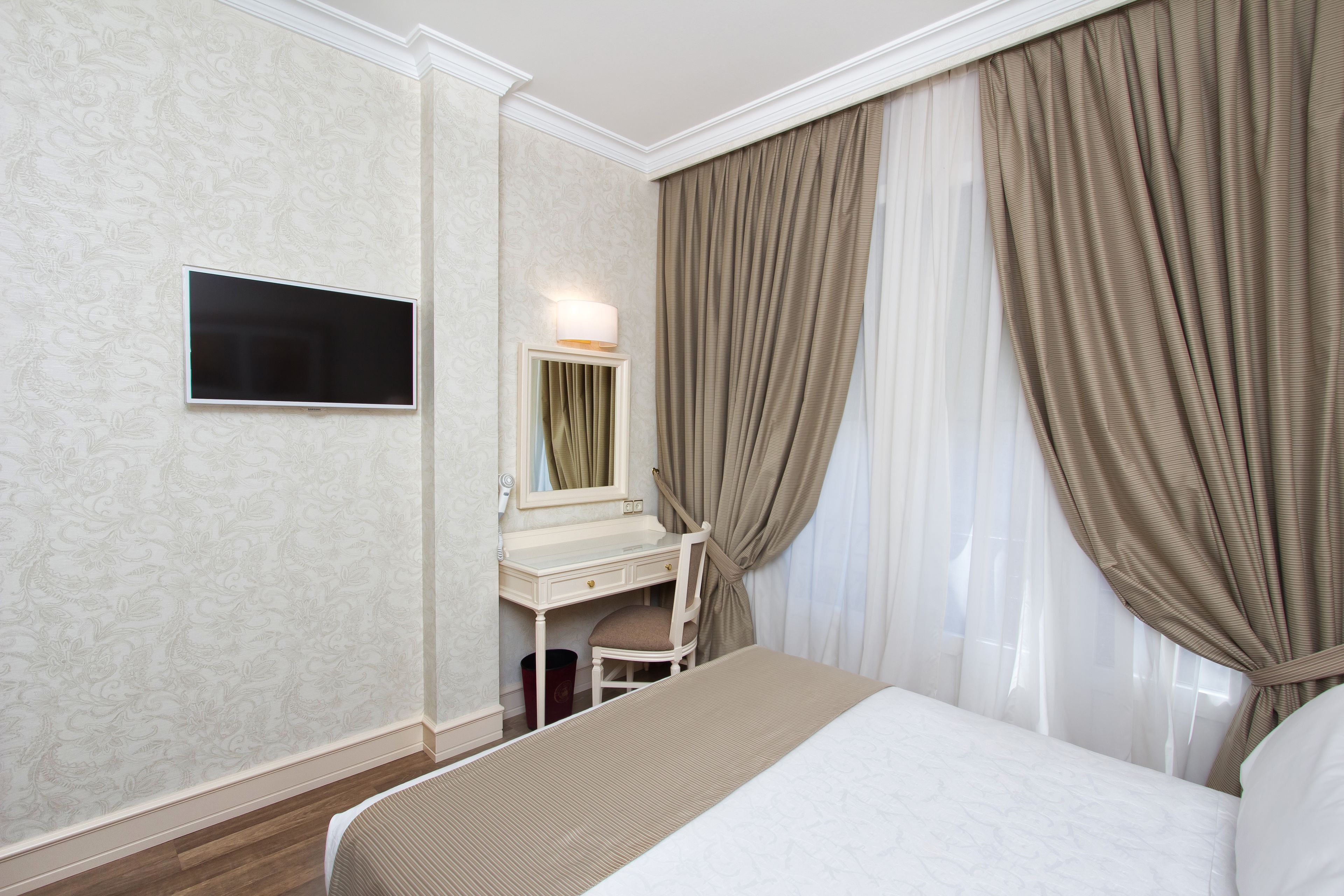 A hotel room with a bed, a desk, a chair, a TV, and curtains.