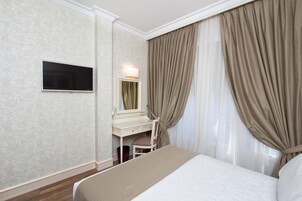 A hotel room with a bed, a desk, a chair, a TV, and curtains.