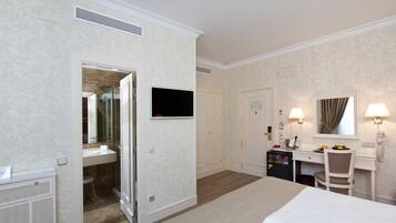 A hotel room with a bed, a desk with a chair, a television, a mirror, and a bathroom with a sink and shower.