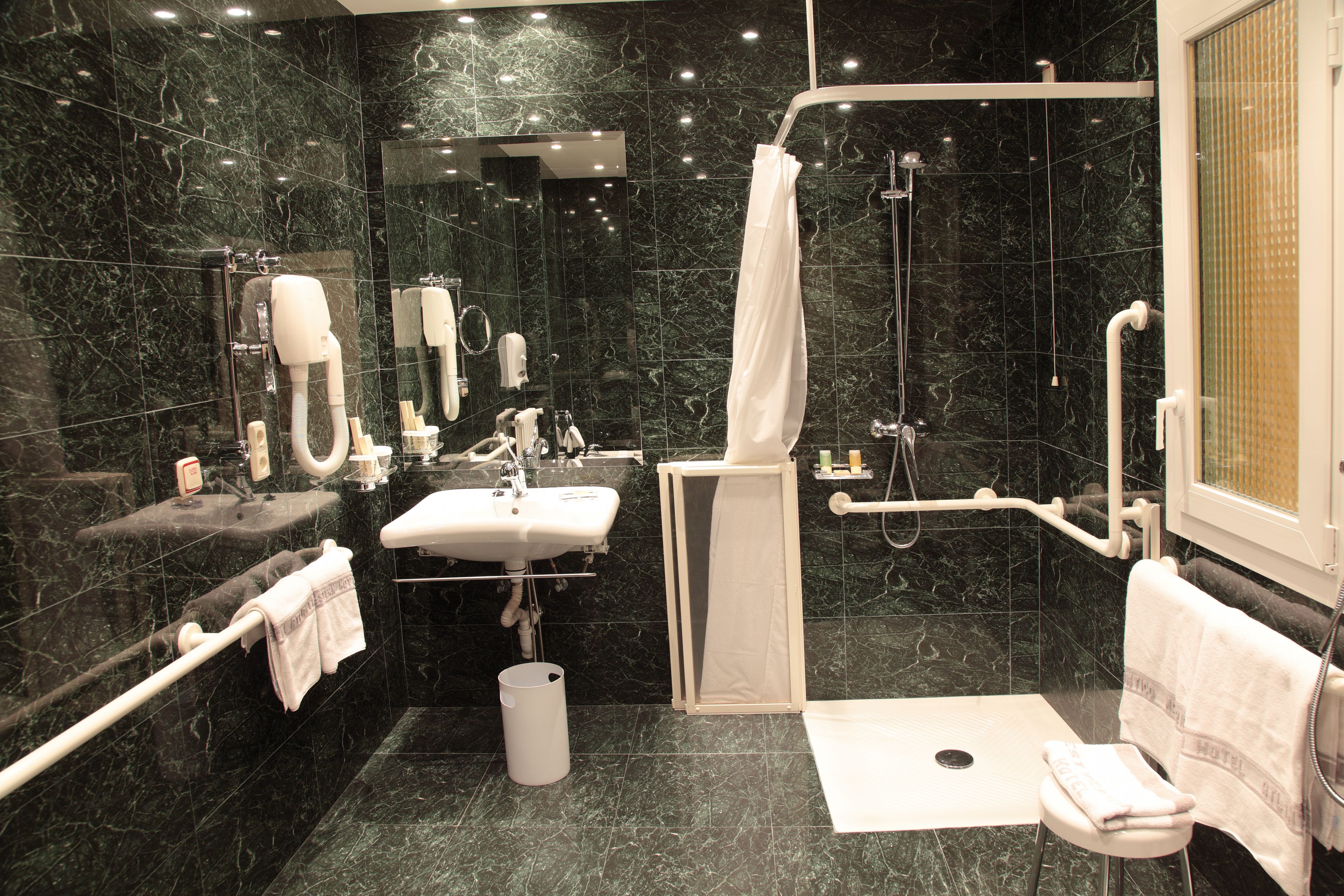 Un baño moderno con piso de mármol, un lavamanos, un espejo, una ducha con puerta de vidrio y un pasamanos.