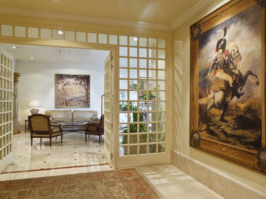 A grand hallway with a large ornate painting, a sofa set, and a decorative gate.