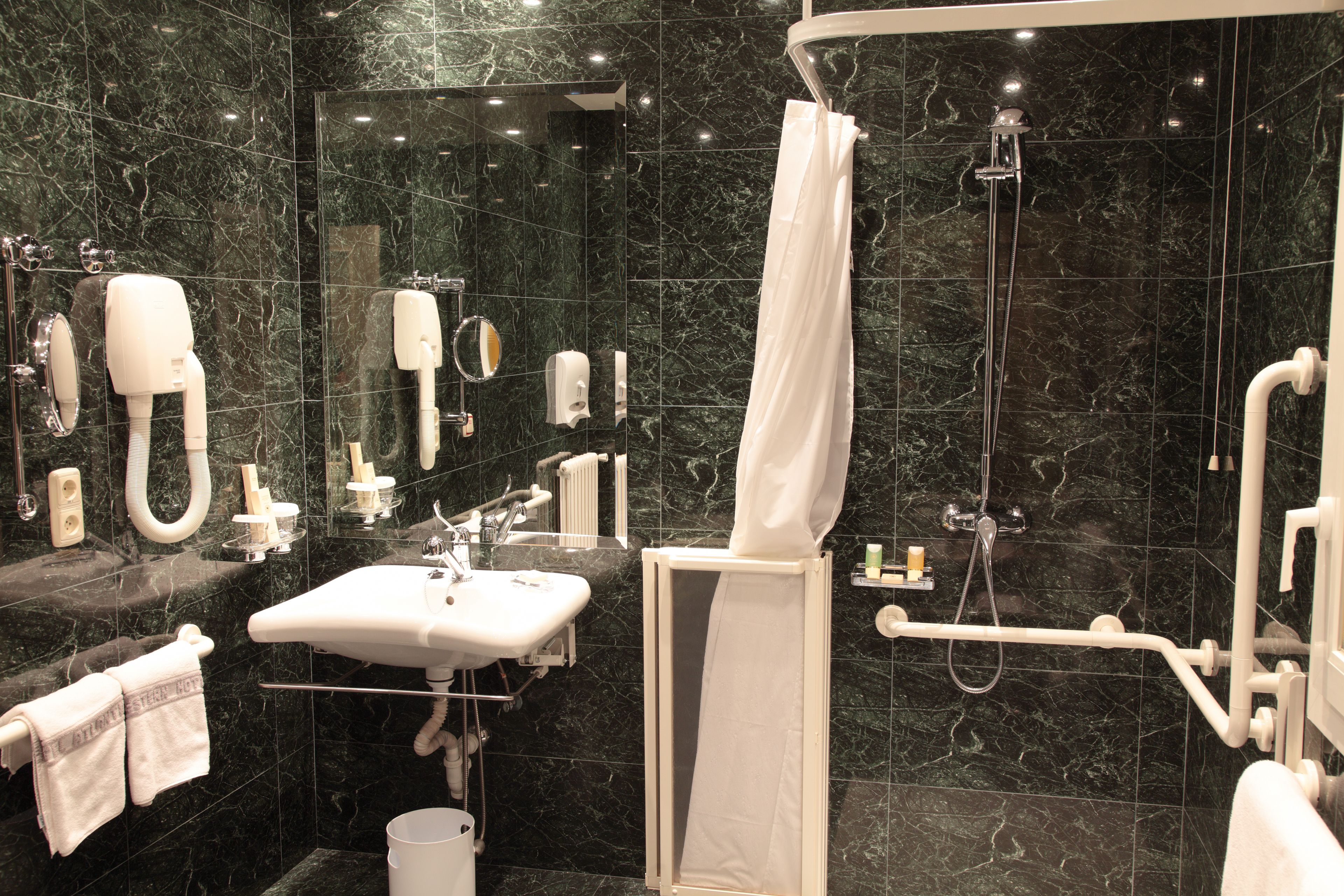 A modern bathroom with a sink, mirror, towel rack, shower, and hand dryer.