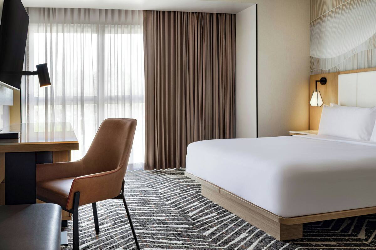 A hotel room with a bed, a desk, a chair, and a lamp.