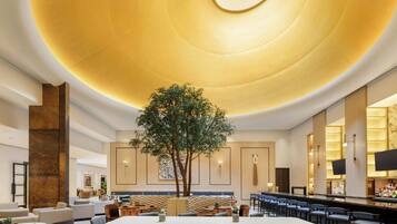En moderne hotellobby med et stort træ, siddepladser og en bar.