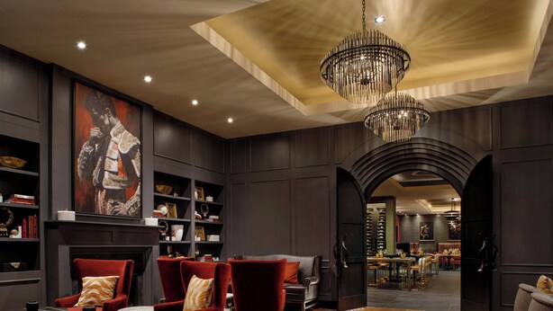 A spacious room with a large wooden table, red armchairs, a chandelier, and a fireplace.