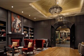 A spacious room with a large wooden table, red armchairs, a chandelier, and a fireplace.