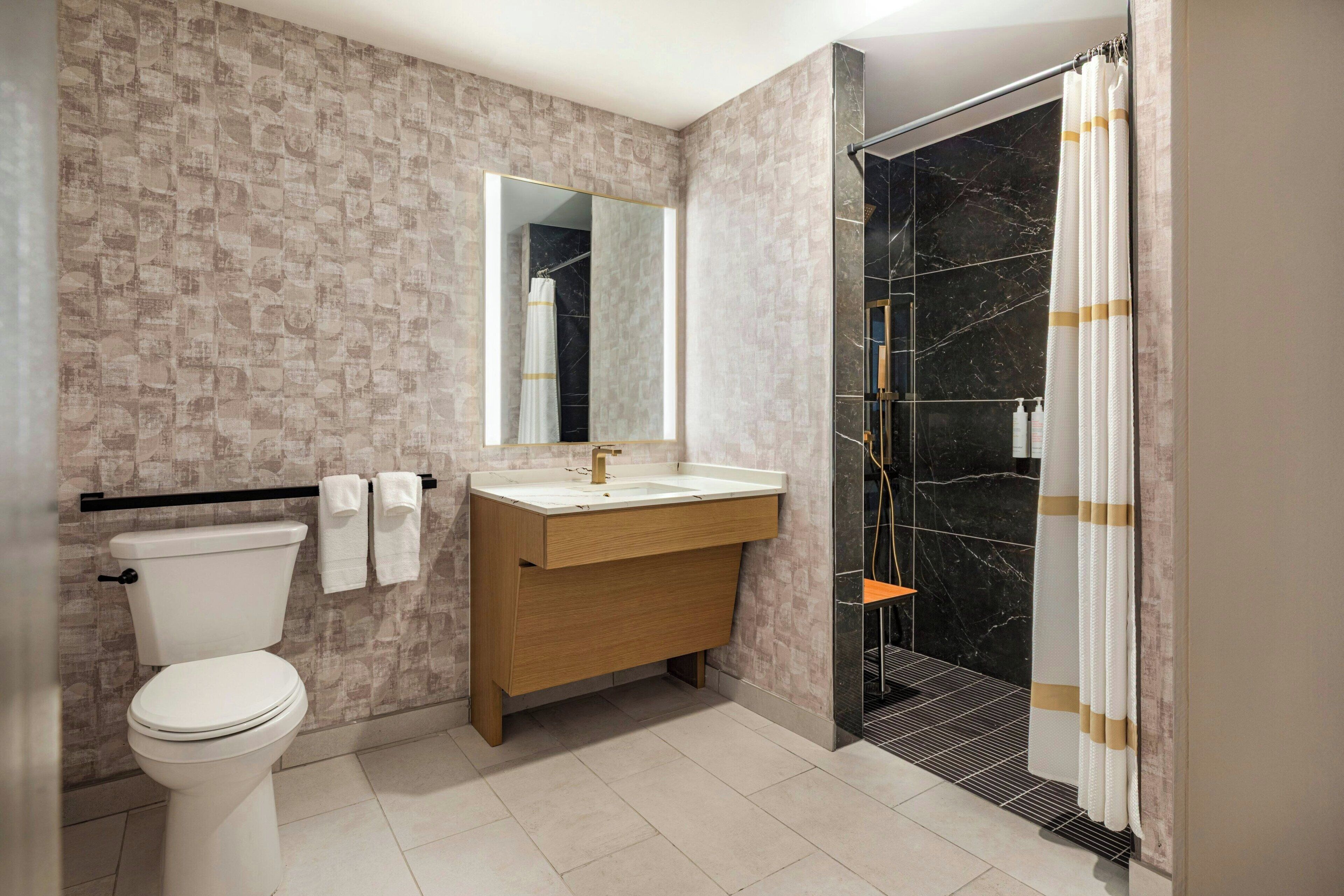 A bathroom with a toilet, sink, mirror, shower, and tiled floor.