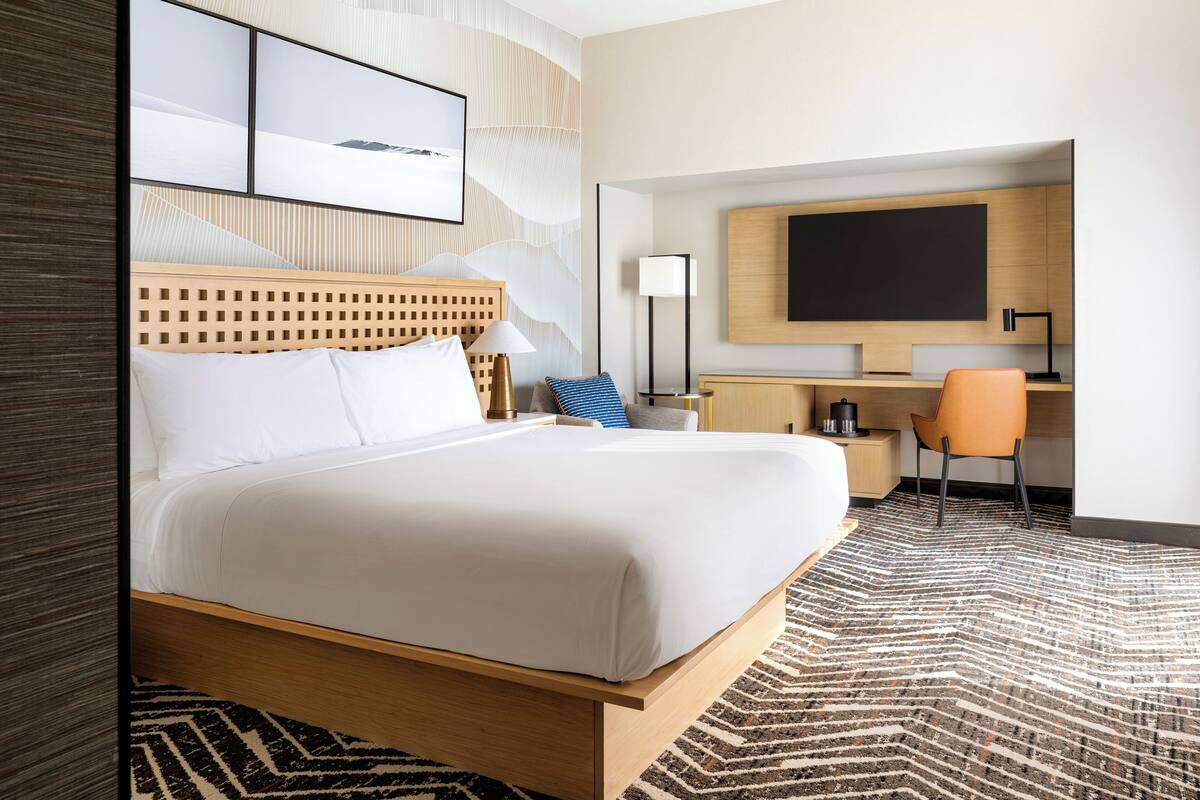 A hotel room with a bed, a desk, a chair, a lamp, and a large mirror.