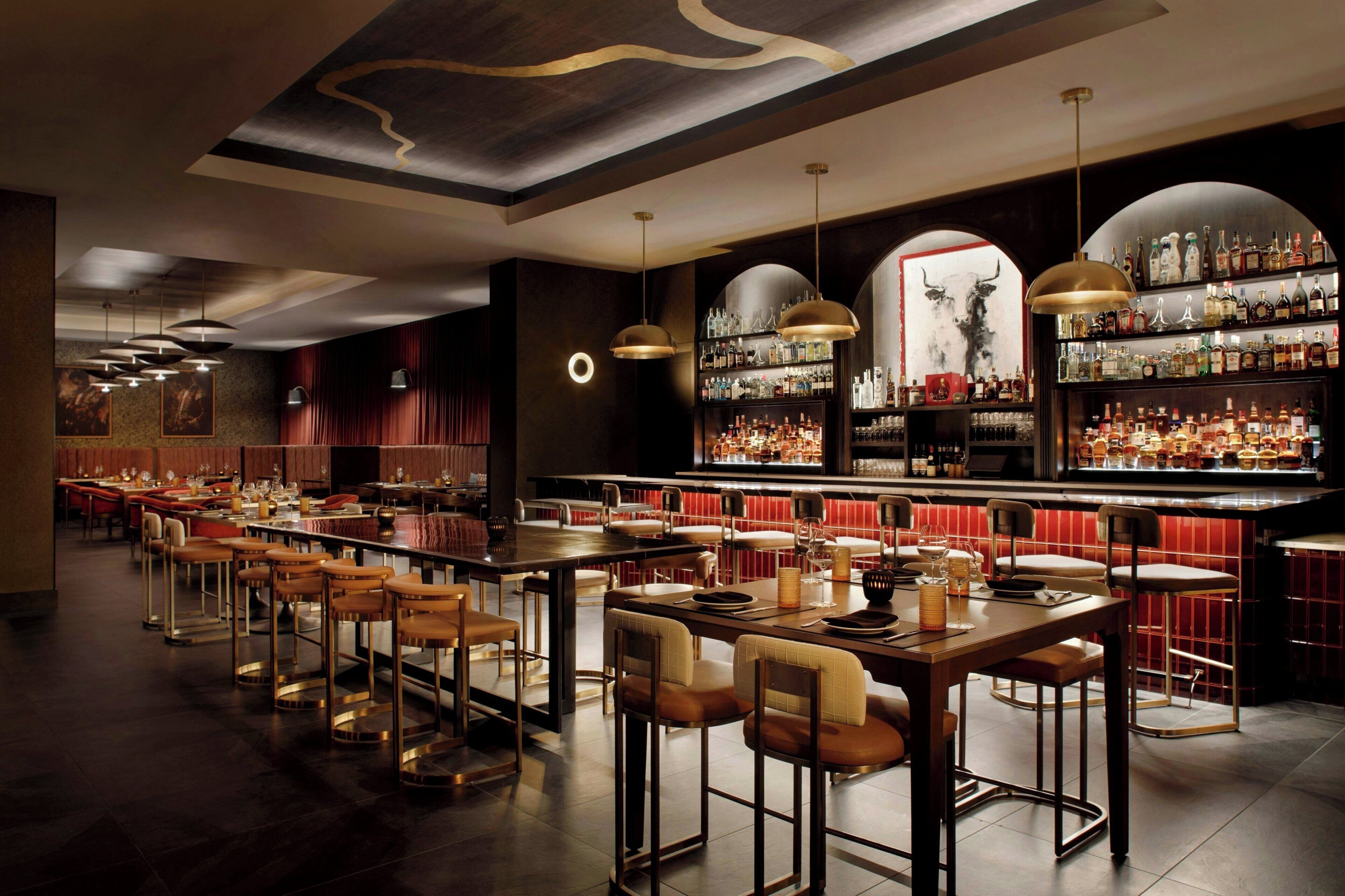 A bar area with multiple seating arrangements, a well-stocked liquor shelf, and pendant lighting.