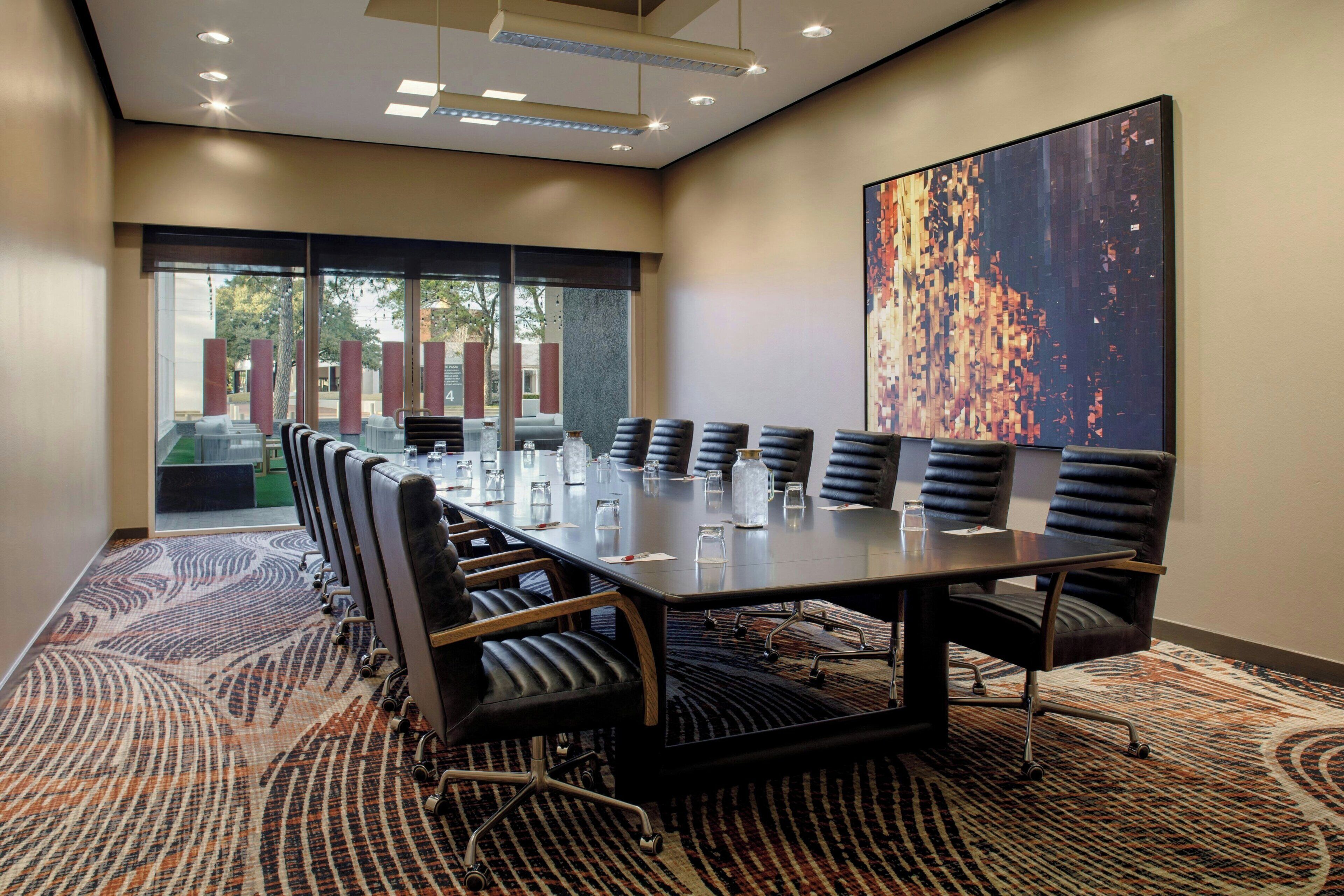 A conference room with a long table, multiple chairs, and a large abstract painting on the wall.