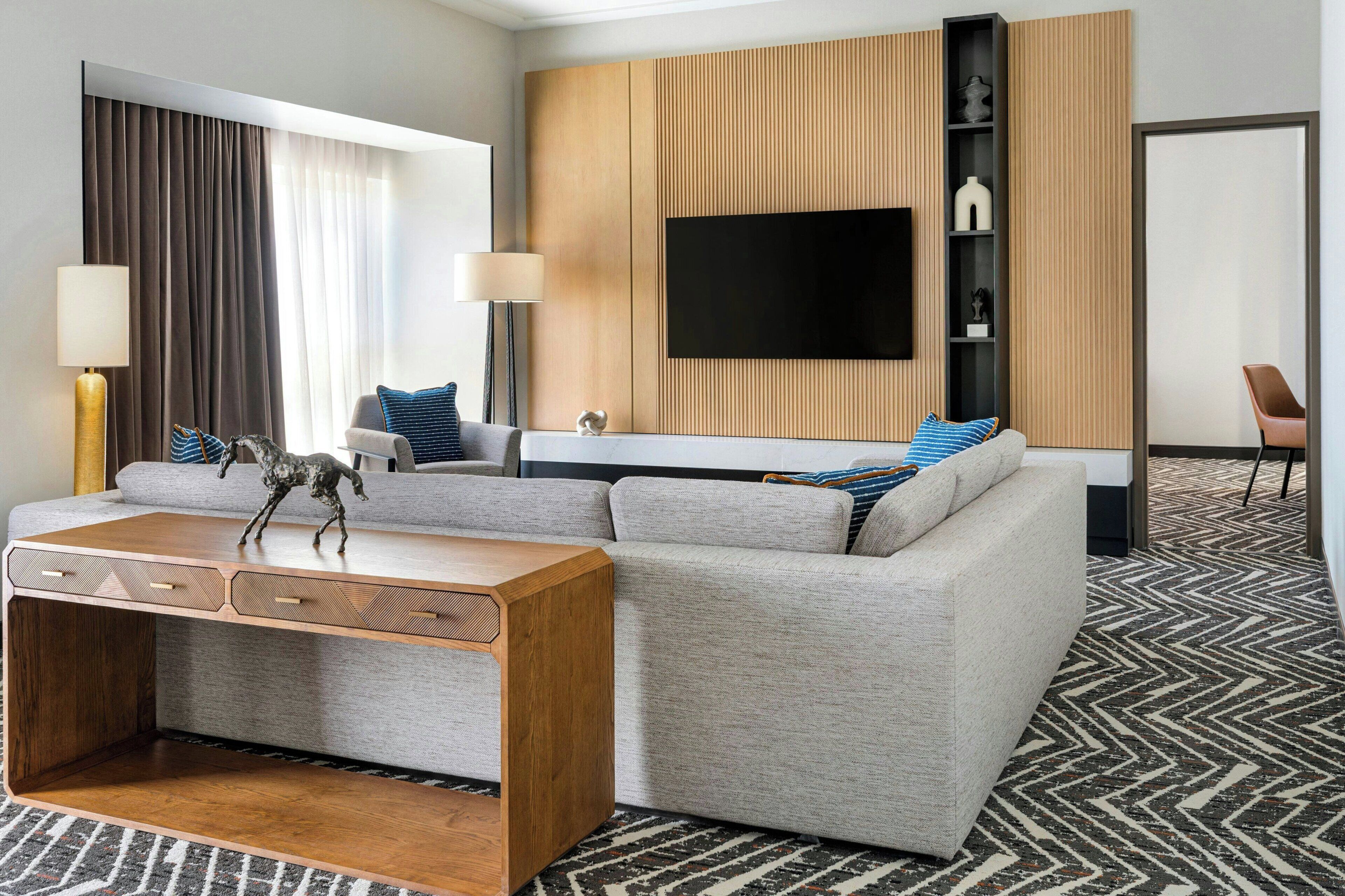 Et moderne hotelværelse med en sofa, et træ sofabord, et fladskærms-tv og et tæppe med et mønster.