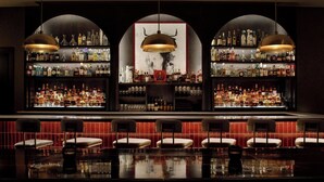 A bar with multiple shelves of liquor bottles, a large mirror, and several bar stools.