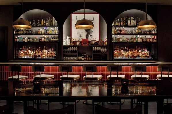 A bar with multiple shelves of liquor bottles, a large mirror, and several bar stools.