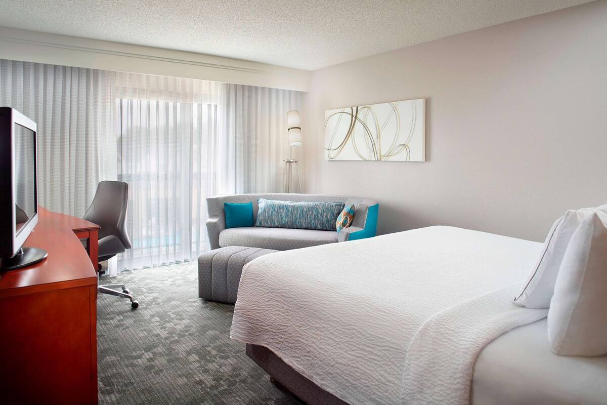 A hotel room with a bed, a desk, a chair, and a large window with curtains.