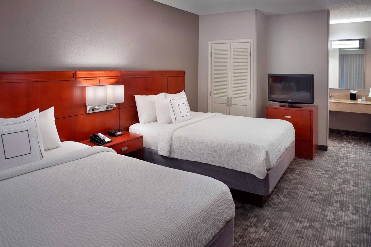 A hotel room with two beds, a TV, a bedside table with a lamp, and a wardrobe.
