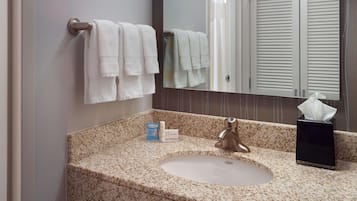 A bathroom with a granite countertop, a sink, a mirror, and towels hanging on a towel rack.