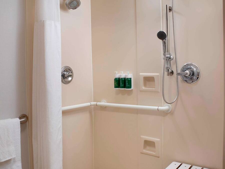 A walk-in shower with a white curtain, grab bars, and a handheld showerhead.