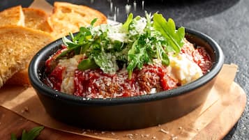 A bowl of tomato-based dish garnished with greens and cheese, accompanied by toasted bread on a wooden board.