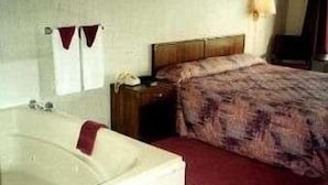 A hotel room with a large bathtub, a wooden nightstand, a bed with a patterned bedspread, and a wall-mounted lamp. - Twinkle Inn (Branson)