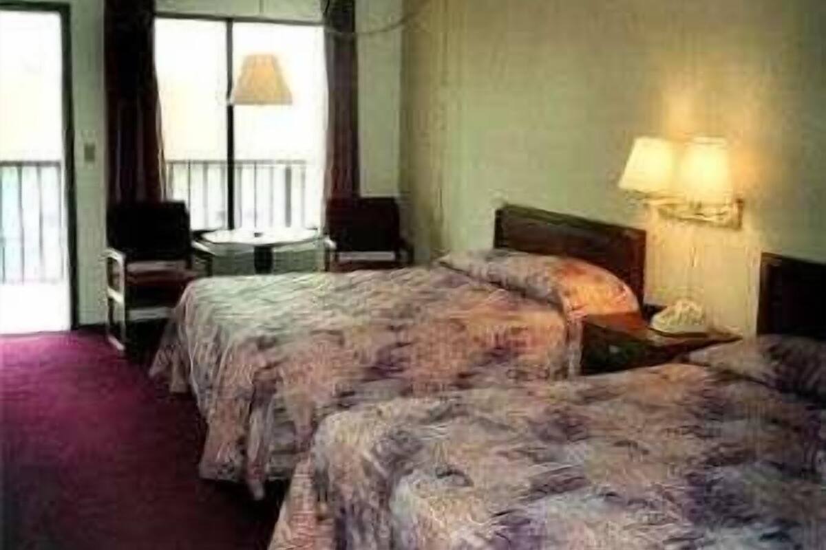 Habitación de hotel con dos camas, una mesita, una silla y un ventanal con cortinas.