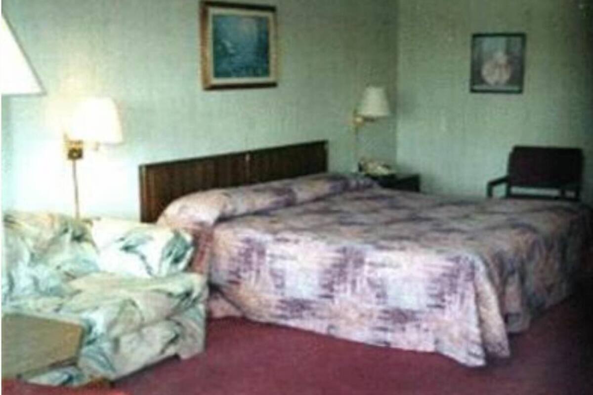 Una habitación de hotel con cama, una silla, una mesita de noche y una lámpara.
