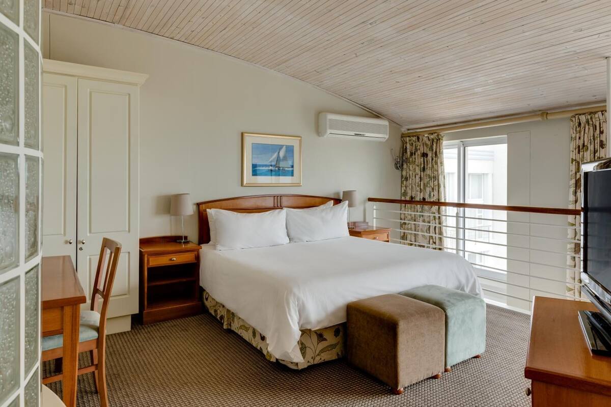 A hotel room with a bed, a desk, a chair, a TV, and a balcony with curtains.