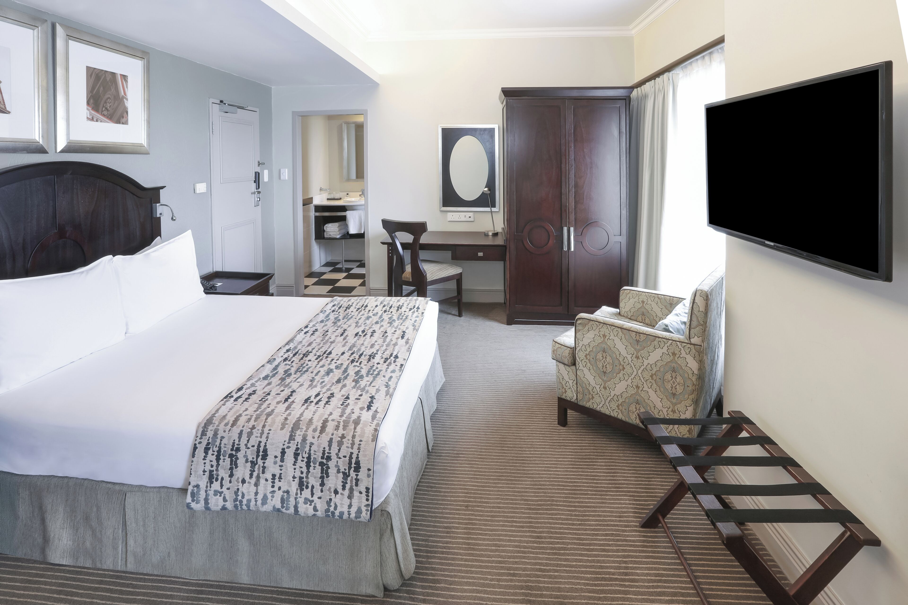 A hotel room with a bed, a desk, a chair, a TV, a wardrobe, and a bathroom.