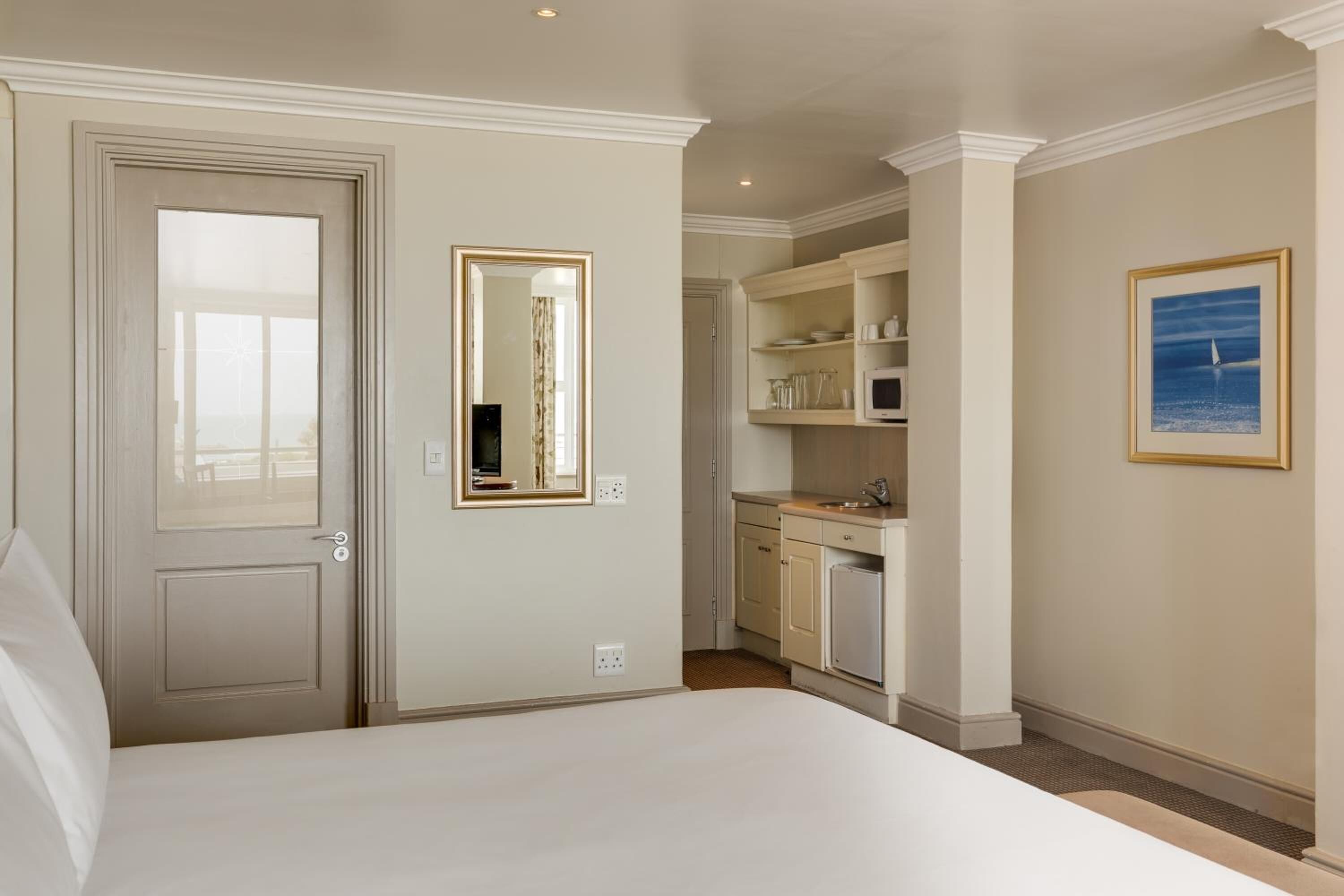 A hotel room with a bed, a bathroom with a mirror, a kitchenette, and a framed picture on the wall.